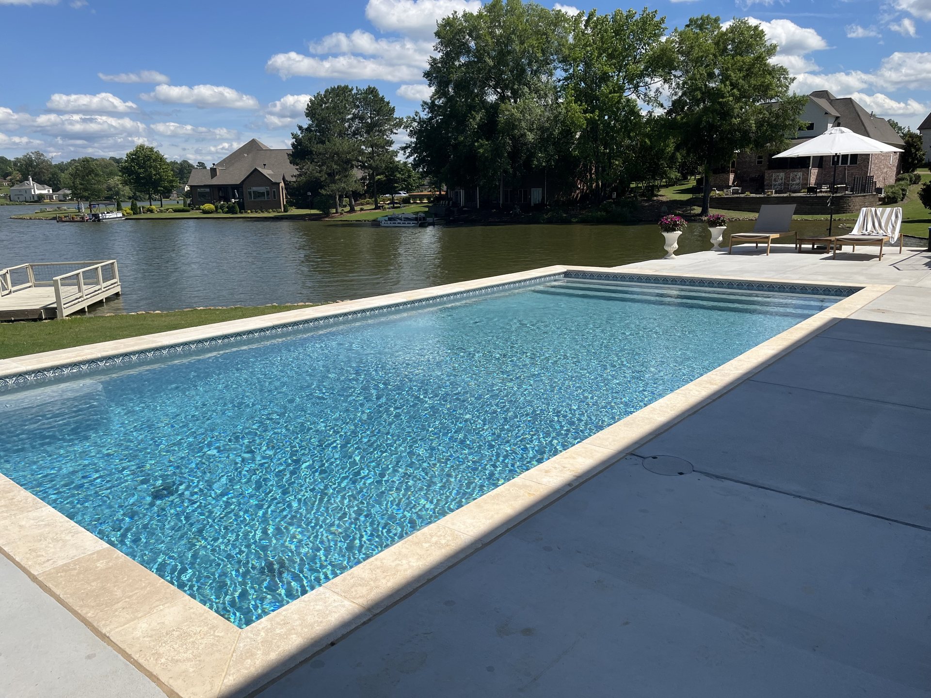 Modern lakefront pool with travertine deck — pool builder website design by Dive In Digital
